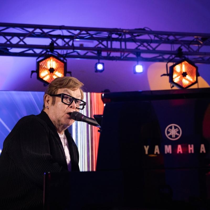 Musician playing a Yamaha piano and singing into a microphone under stage lighting.