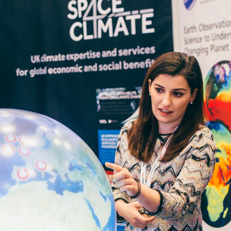 Presenter explaining climate data using a digital globe at a Space4Climate exhibition booth.