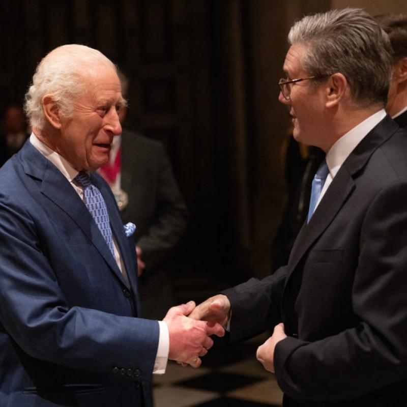 Two men in suits shaking hands at a formal event in a dimly lit venue.