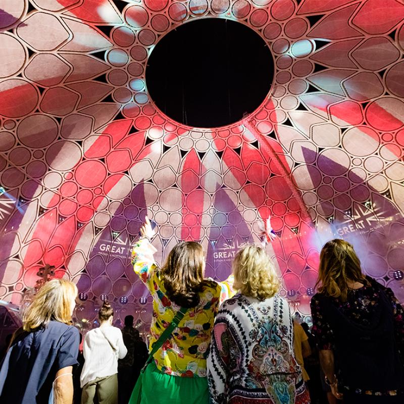 People admiring a colorful, illuminated dome structure during a lively event with intricate patterns and vibrant lighting.